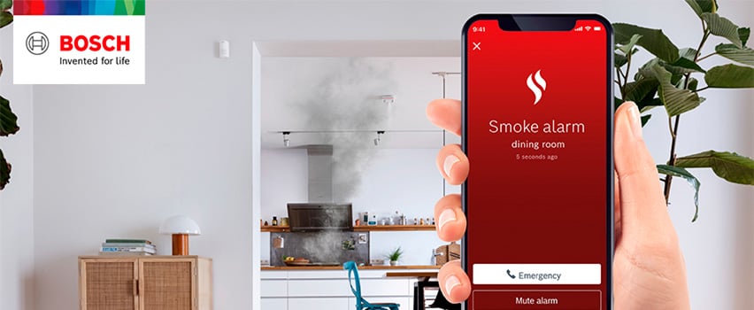 Bosch Smart Home App zeigt Rauchmelder-Benachrichtigung aus Esszimmer mit Notruf-Taste und Rauch aus Küche im Hintergrund
